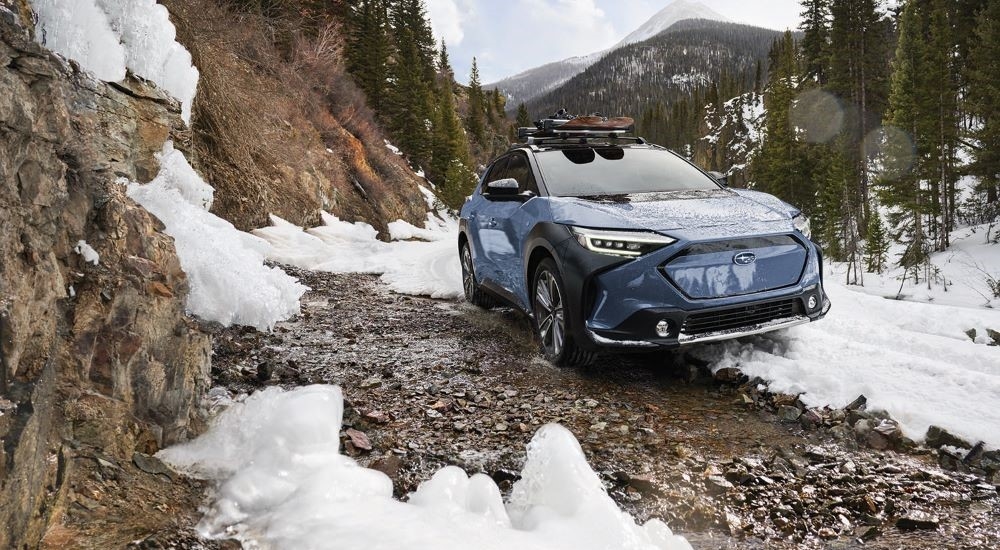 A blue 2023 Subaru Solterra is shown on a snowy mountain trail.