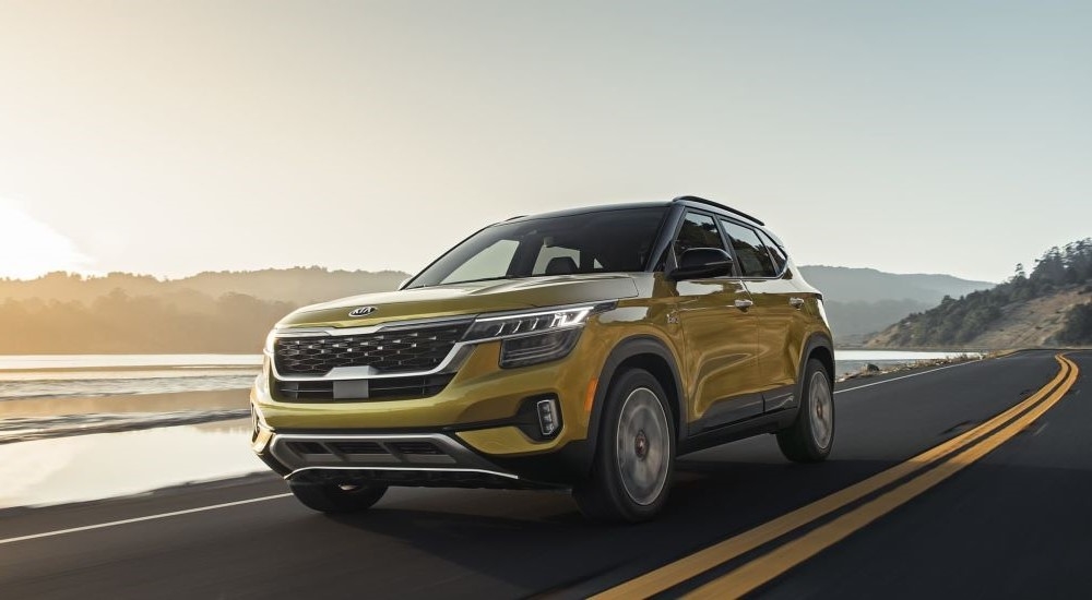 A yellow 2021 Kia Seltos is shown driving past a lake after visiting a used Kia dealer near Port Lavaca.