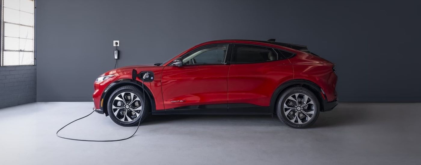 A red 2023 Ford Mustang Mach-E is shown from the side charging in a garage.