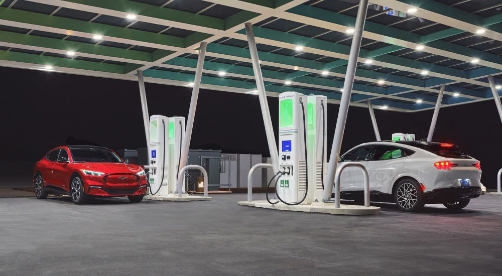 A red and a white 2022 Ford Mustang Mach-E are shown charging.