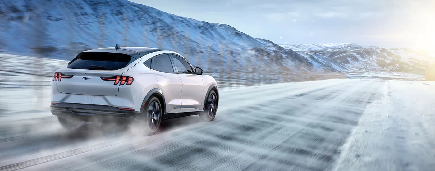 A white 2022 Ford Mustang Mach-E Premium is shown from the rear driving on a snowy road after visiting a new Ford dealership.