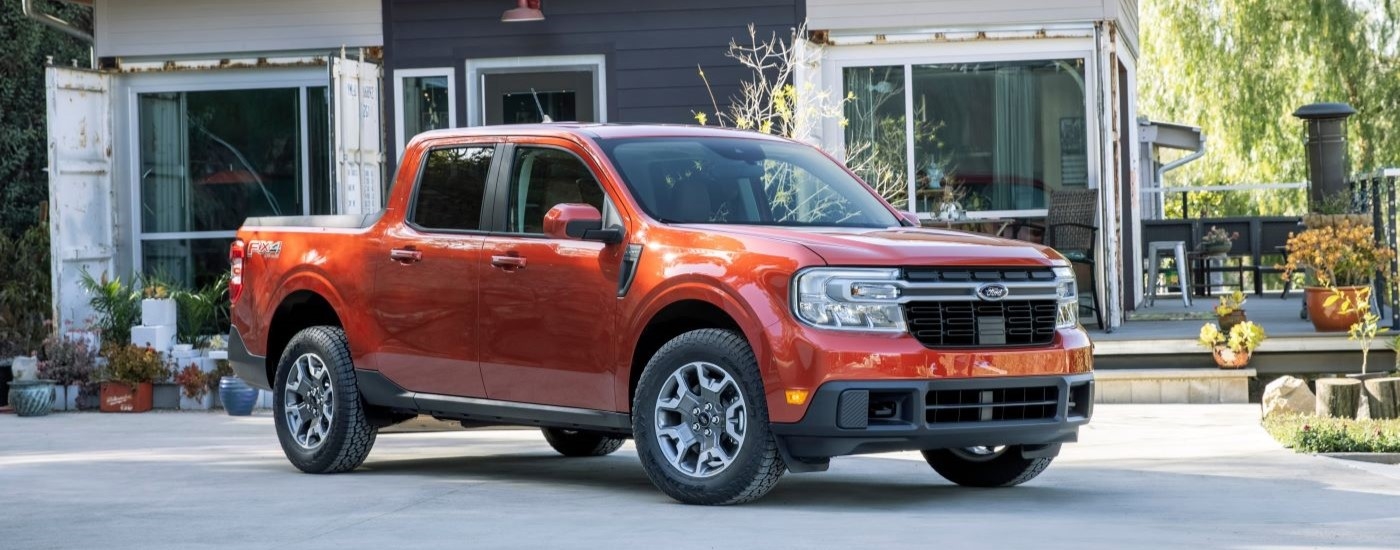 A red 2022 Ford Maverick Lariat is shown from a side angle parked in front of a house.