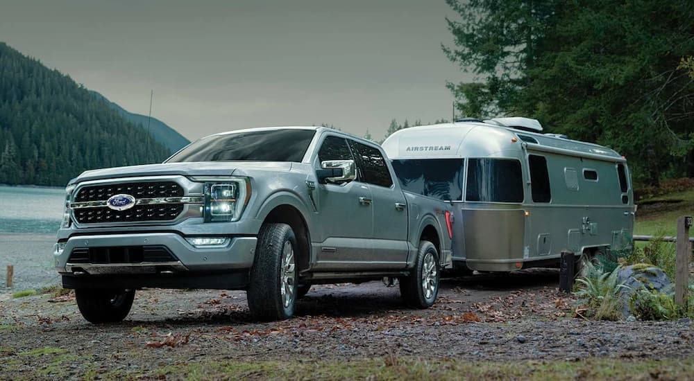 A silver 2022 Ford F-150 is shown towing an Airstream trailer next to a lake.