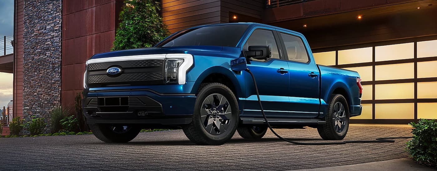A blue 2022 Ford F-150 Lightning is shown charging in front of a garage.