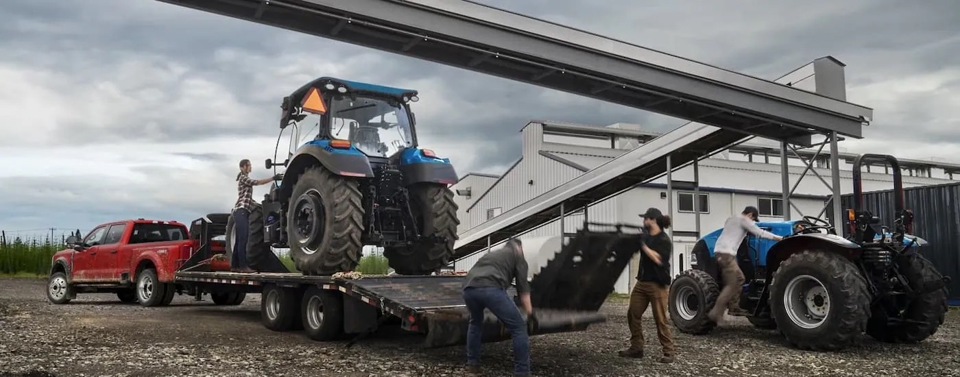 A red 2024 Ford F-350 Super Duty is shown hooked up to a trailer with a large blue tractor.