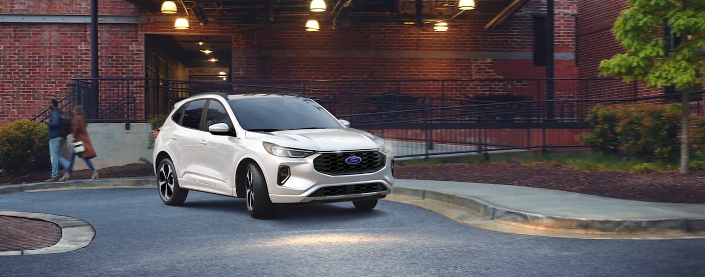 A white 2023 Ford Escape ST-Line is shown driving in a parking lot.