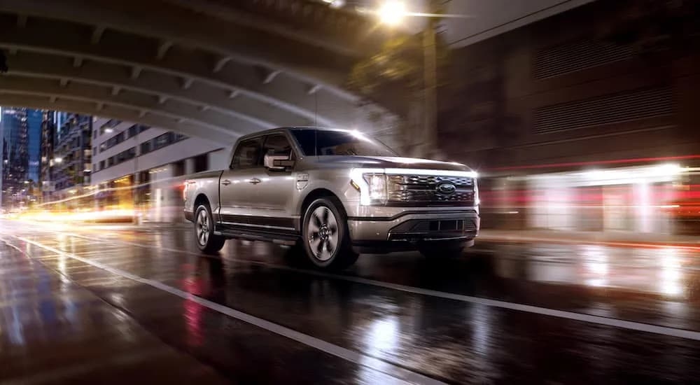 A silver 2022 Ford F-150 Lightning Platinum is shown driving on a wet city street at night.