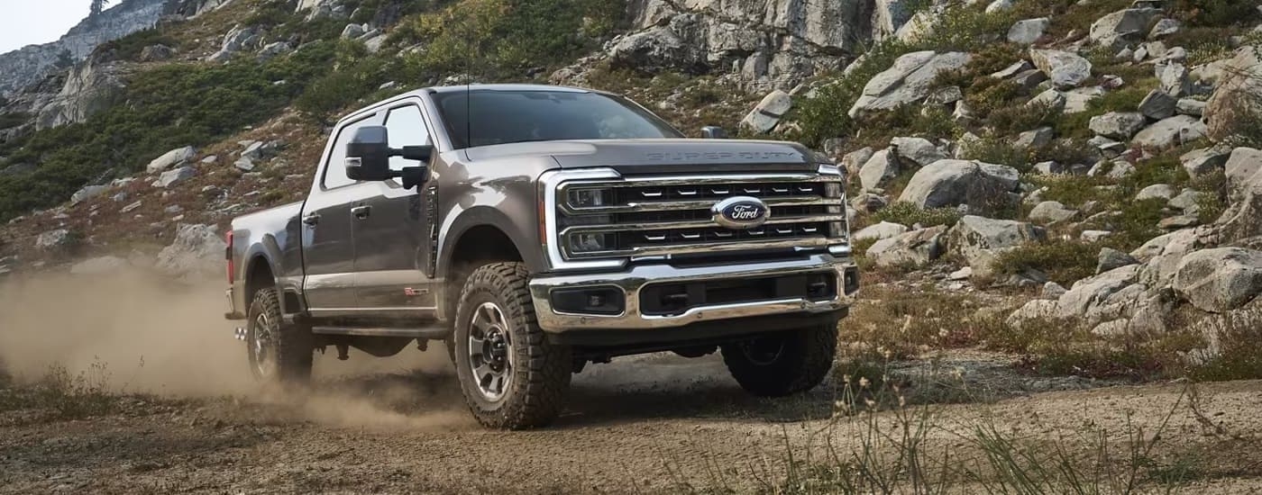 A grey 2023 Ford F-250 is shown driving on a dusty dirt road.