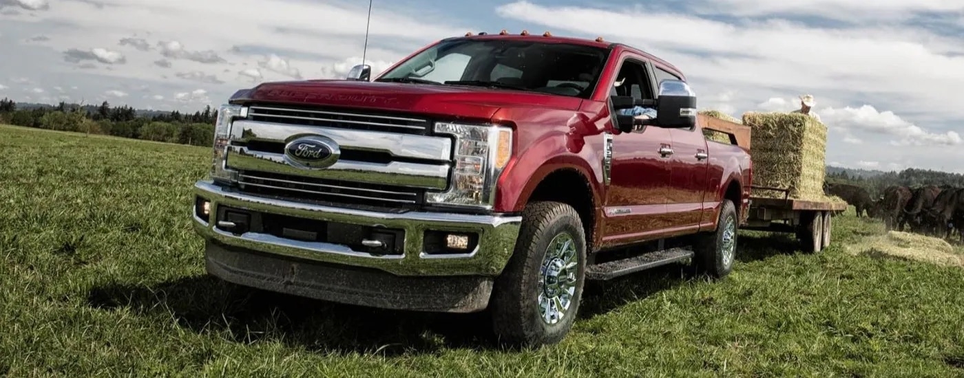 A red 2017 Ford F-250 is shown towing a trailer of hay bales through a field.