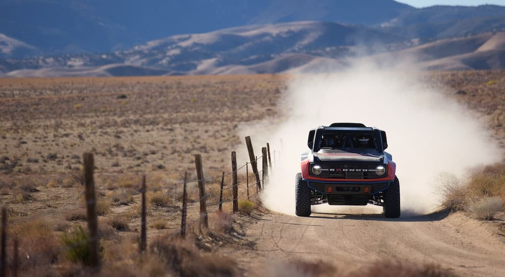 A red 2023 Ford Bronco DR is shown driving on a dusty trail after leaving a new Ford dealership.