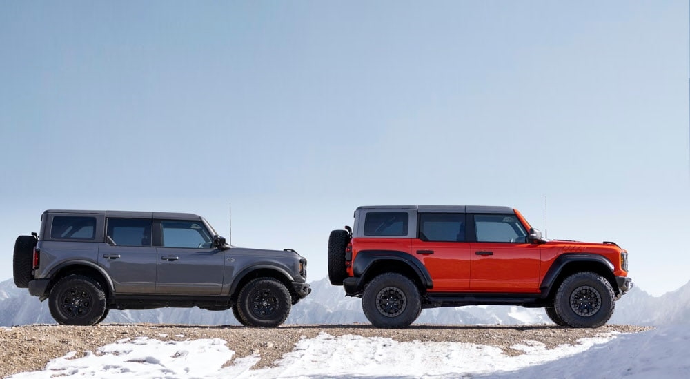 A grey 2023 Ford Bronco Wildtrak and a red Bronco Raptor are shown from the side.
