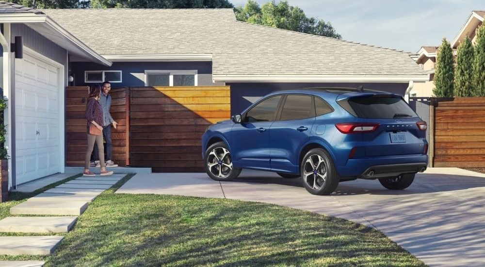 A blue 2023 Ford Escape is shown from a rear angle while parked in a driveway in front of a home.