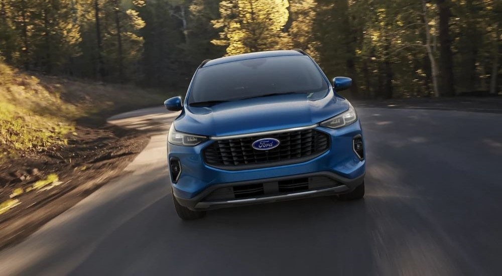 A blue 2023 Ford Escape is shown from the front while driving on a winding forest road.