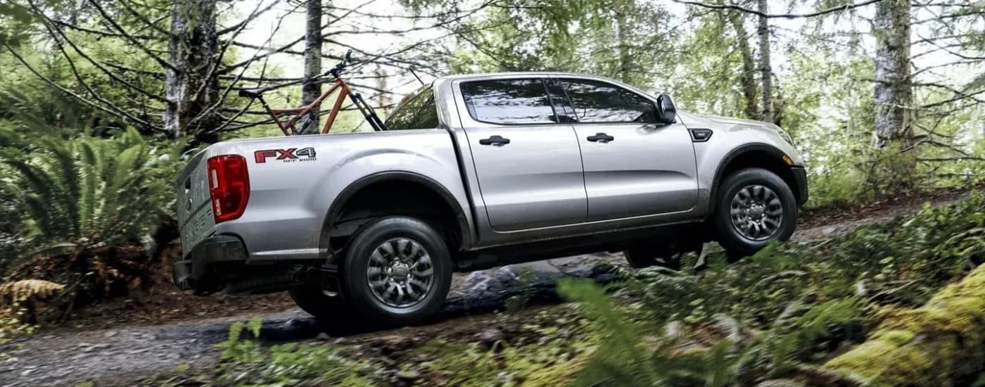 A silver 2023 Ford Ranger XLT FX4 is shown driving on a trail in the woods.