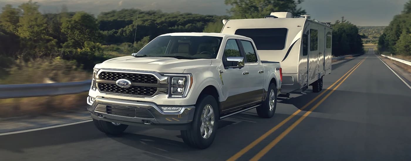 A white 2022 Ford F-150 is shown towing a camper after leaving a Ford F-150 dealer.