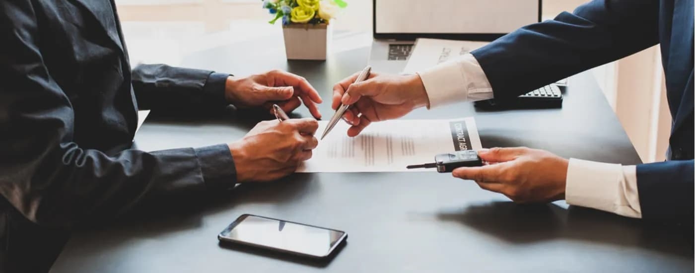 A salesman is shown going over paperwork a customer needs to sell their car.