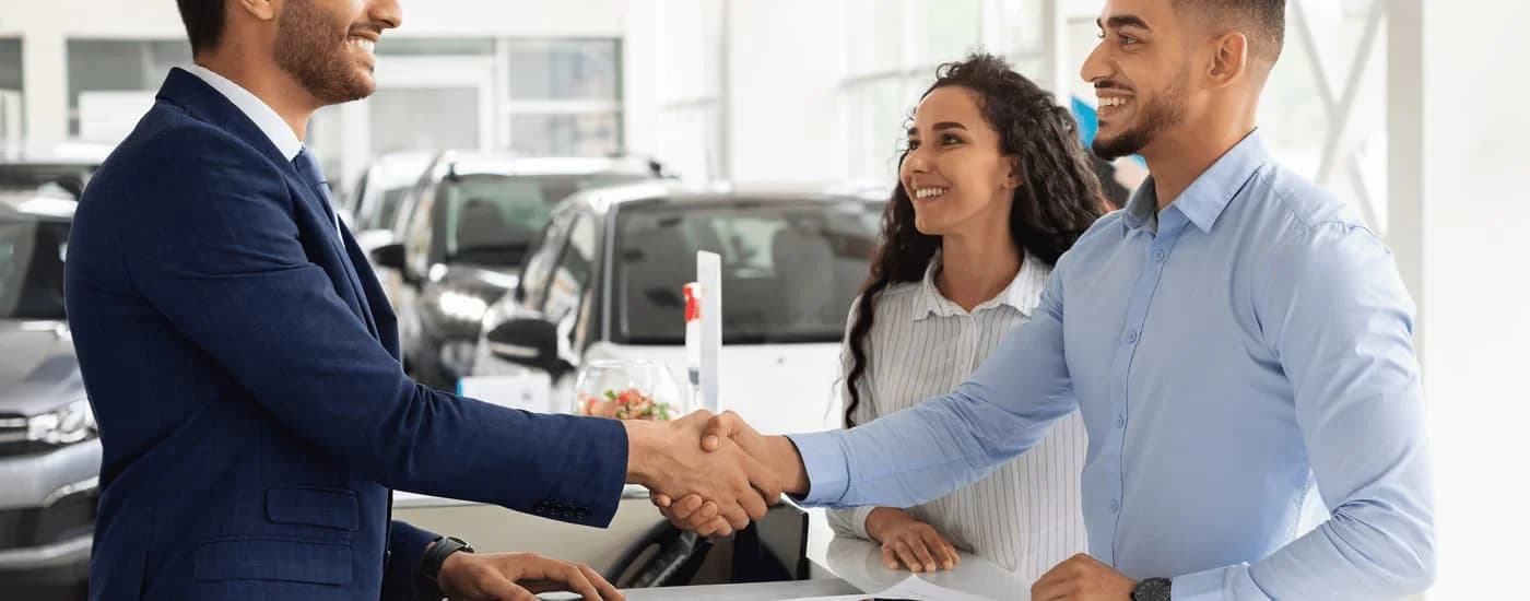 A couple is shown shaking hands with a salesman after asking how to 'sell my car.'