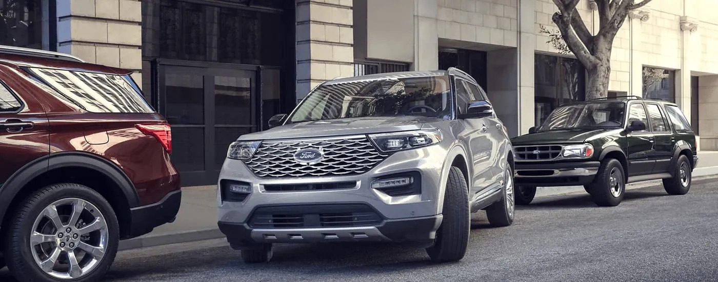 A silver 2023 Ford Explorer for sale is shown pulling out of a parking spot on the side of a street.