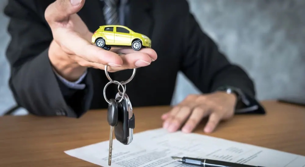 A salesman is shown holding a toy car and a set of car keys.