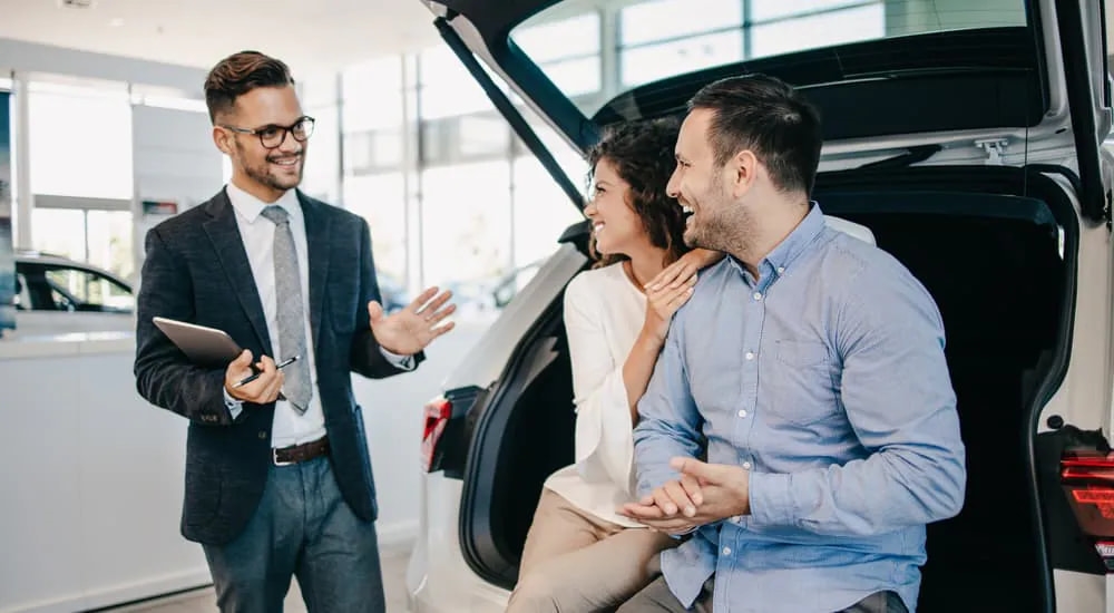 A salesman is shown speaking to a couple about their vehicle's trade-in value.