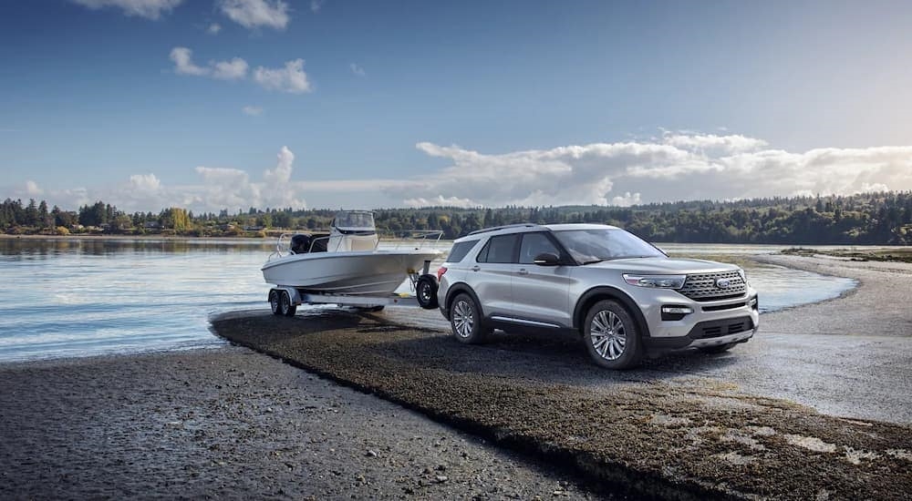 A silver 2023 Ford Explorer Platinum Hybrid is shown towing a boat out of a lake.