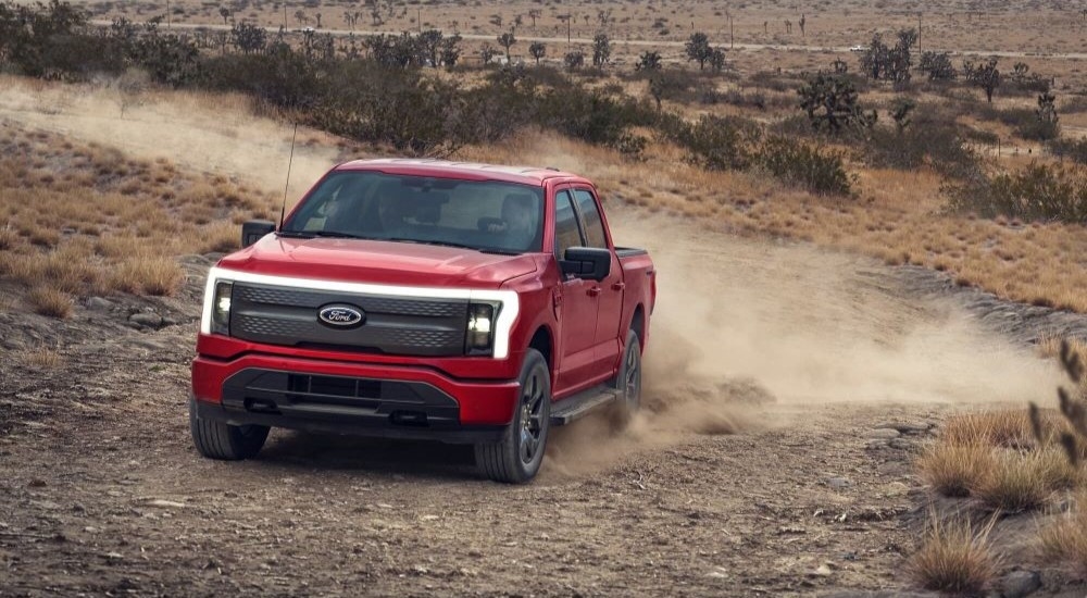 A red 2022 Ford F-150 Lightning is shown from the front driving on a dirt road.