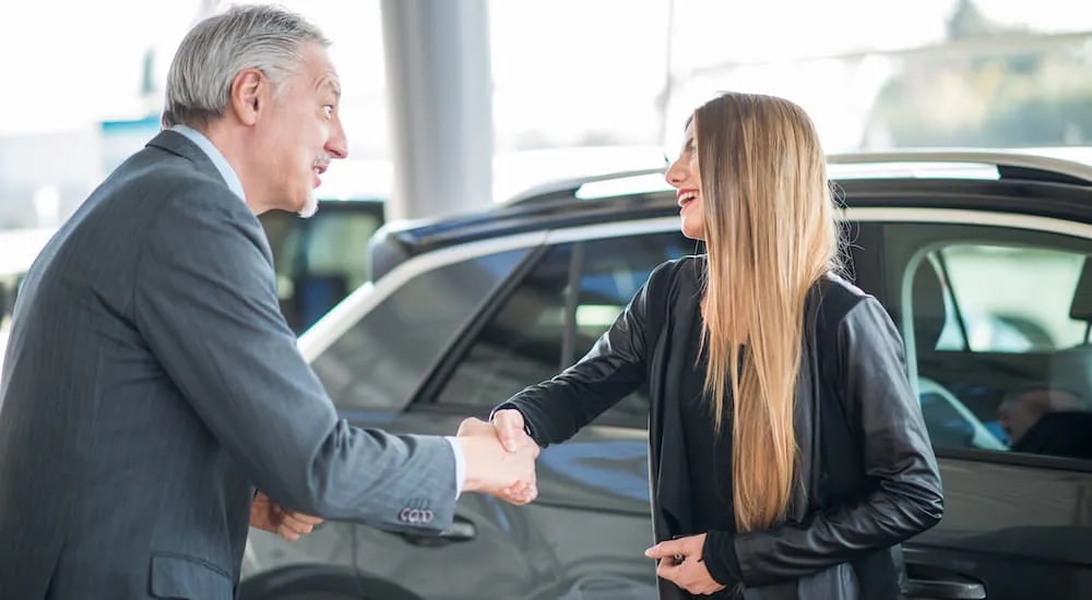 A woman is shown shaking hands with a salesman after selling her car.
