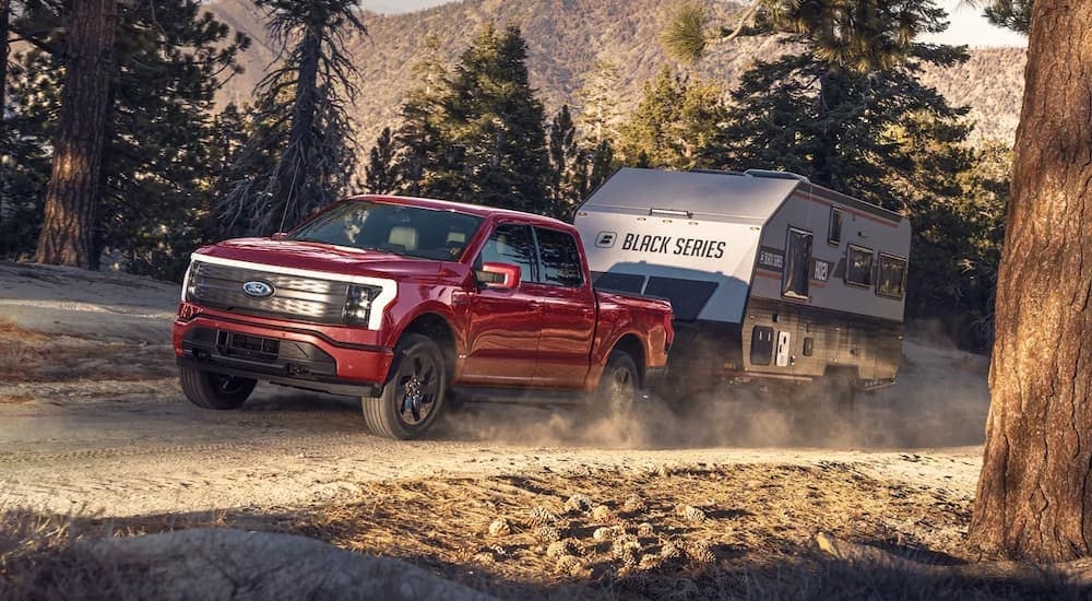 A red 2022 Ford F-150 Lightning is shown towing a camper on a dirt trail after visiting a Ford F-150 dealer.