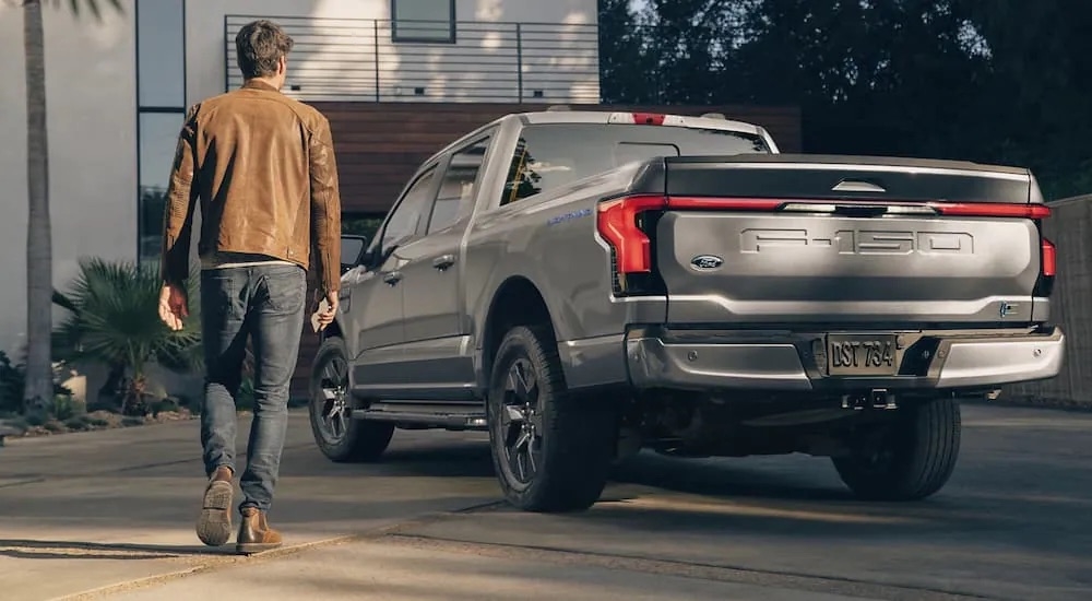 A silver 2022 Ford F-150 Lightning is shown from the rear on the driveway of a modern house.