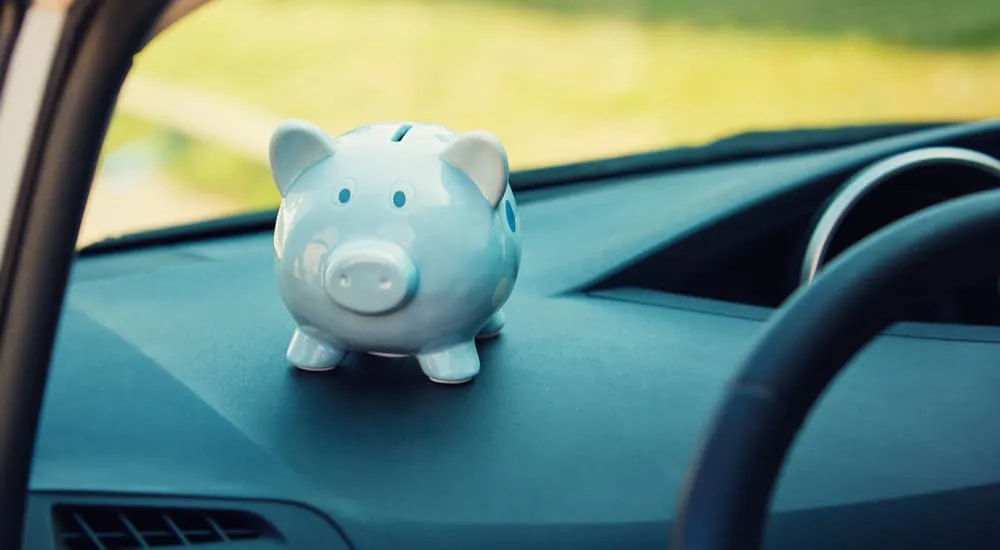 A white piggy bank is shown on the dashboard of a vehicle.
