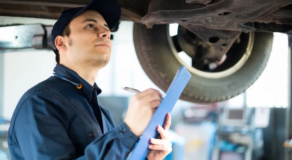 A mechanic is shown inspecting the underneath of a vehicle.