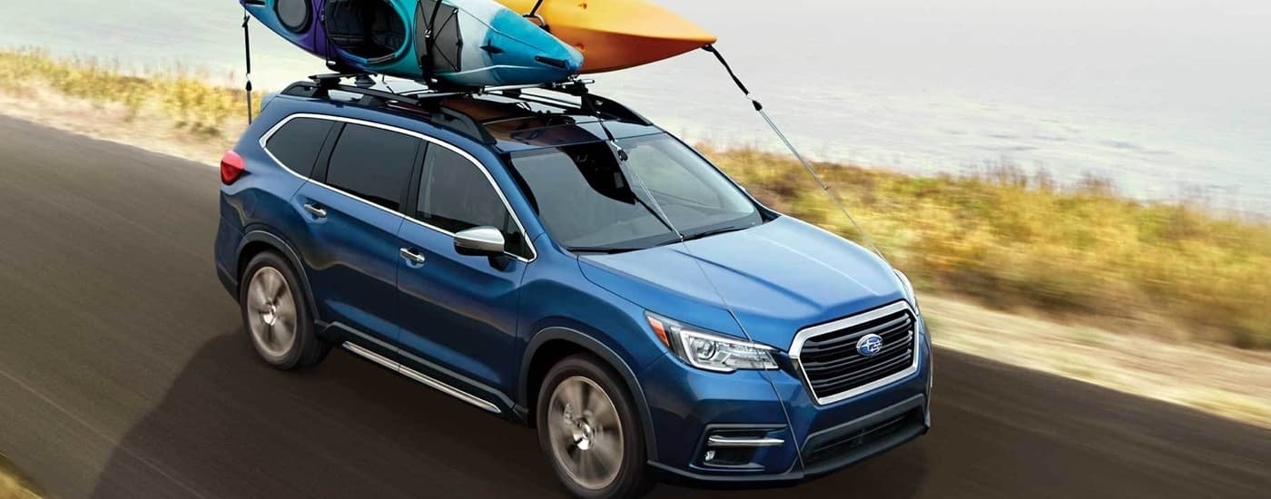 A blue 2022 Subaru Ascent Touring is shown driving with kayaks on the roof after leaving a used SUV dealer.