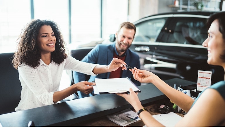 Woman handing vehicle paperwork to a saleswoman