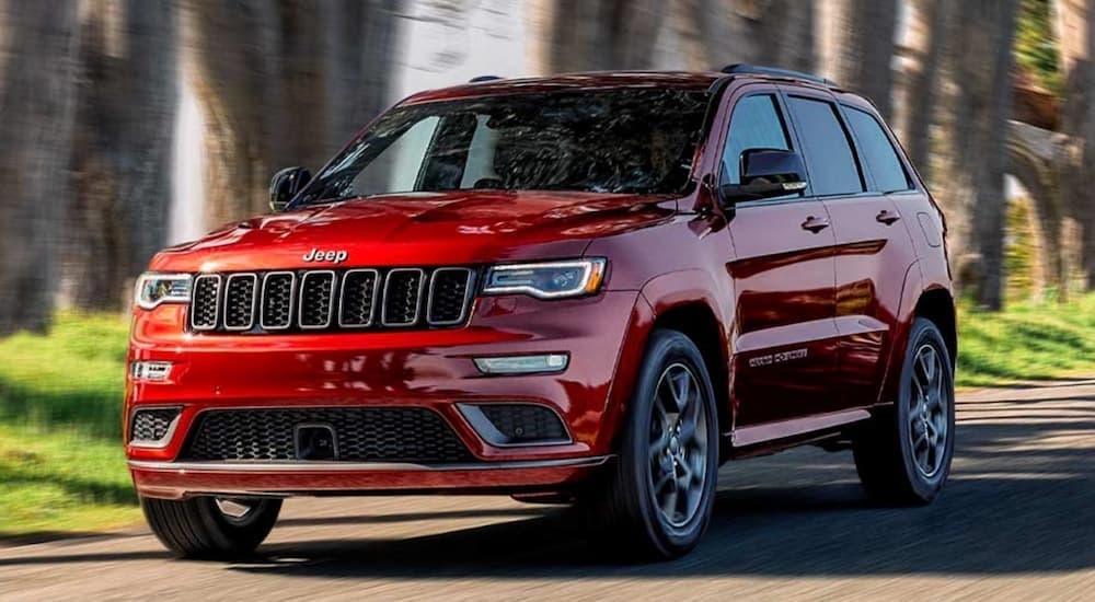 A red 2020 Jeep Grand Cherokee driving on a tree-lined road after leaving a used SUV dealer.