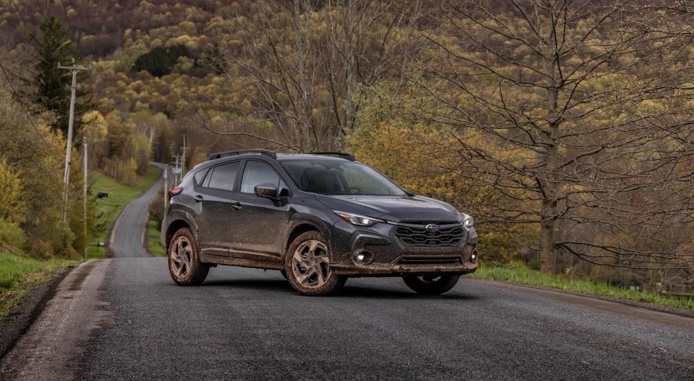 A grey 2024 Subaru Crosstrek Limited is shown parked on a tree-lined road after leaving a car dealership.