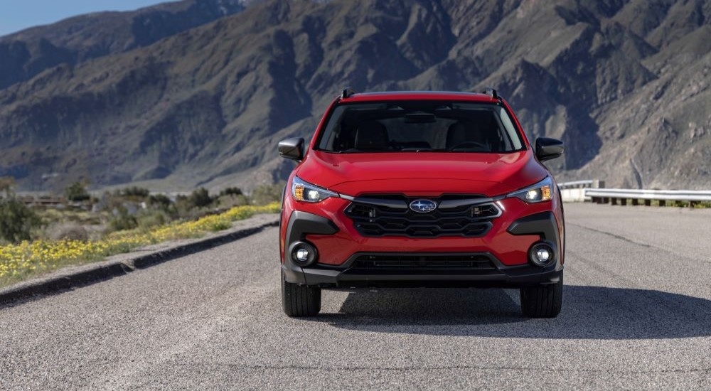 A red 2024 Subaru Crosstrek Premium is shown on a road near mountains.