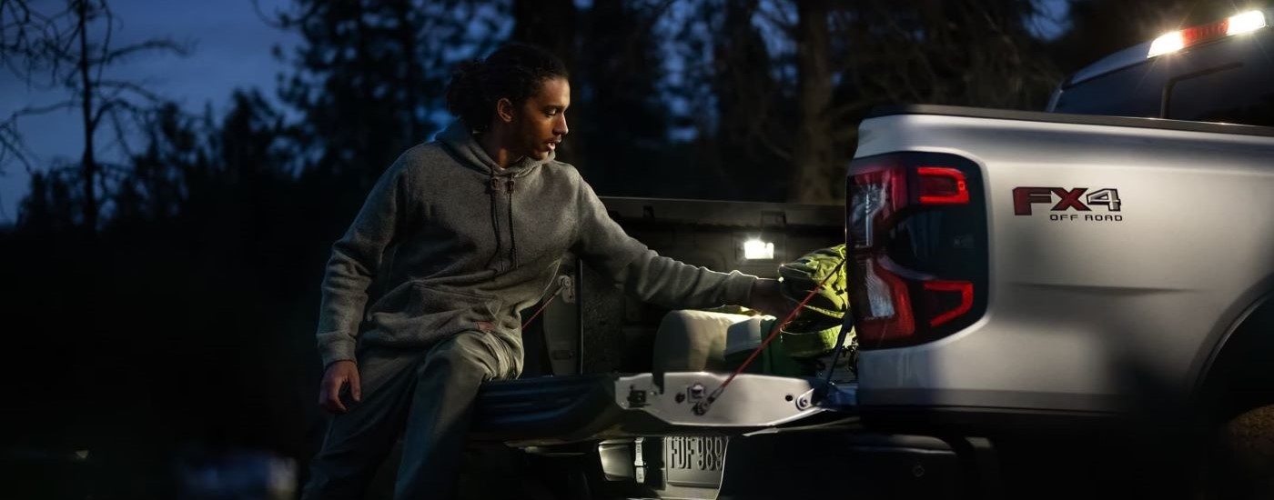 A person is shown grabbing gear from the bed of a silver 2024 Ford Ranger for sale.