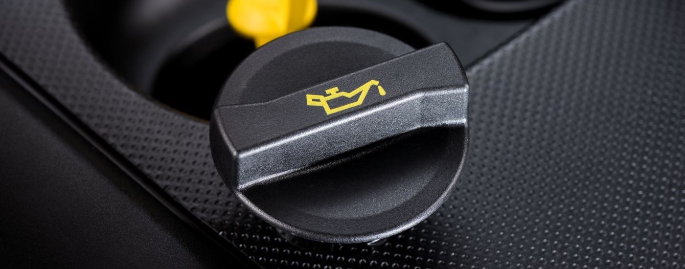 A close up shows a black oil cap sitting on an engine cover.