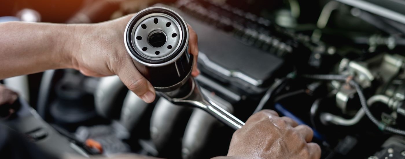 A close up shows a mechanic holding a black oil filter and sockey wrench.