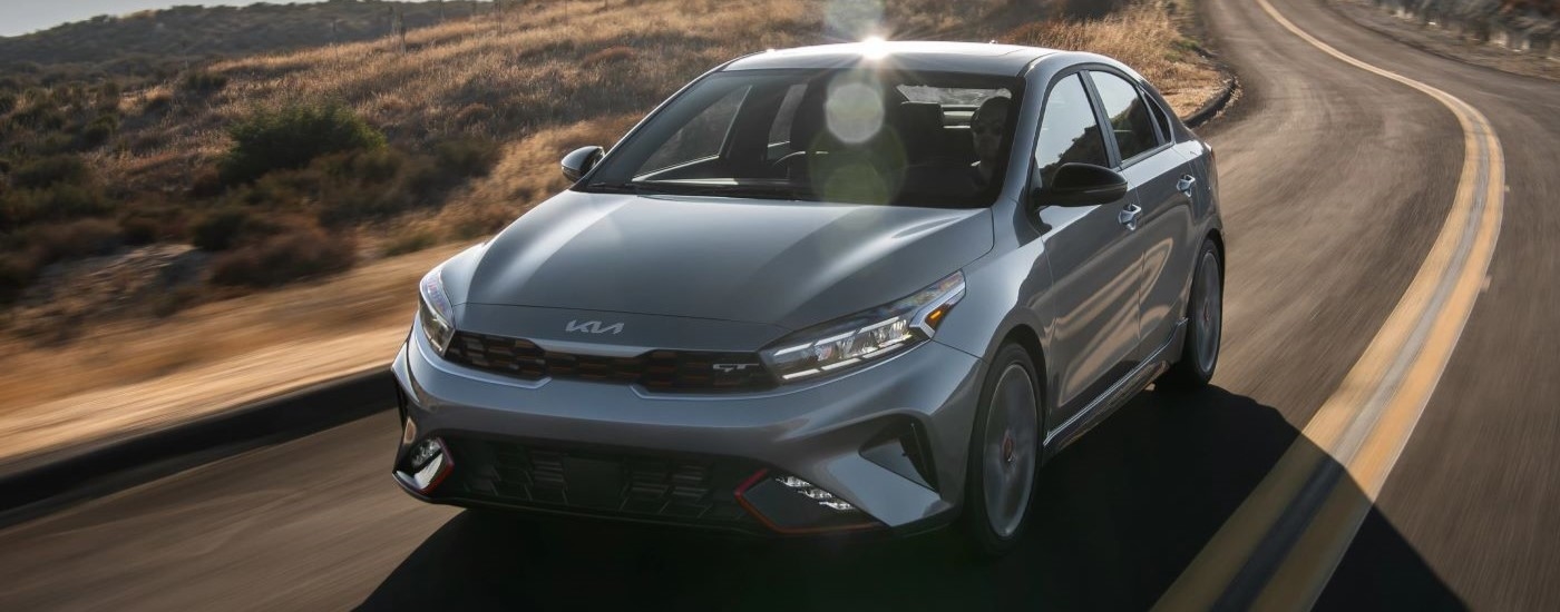 A silver 2023 Kia Forte GT is shown driving on a winding road after visiting a San Antonio Kia dealer.