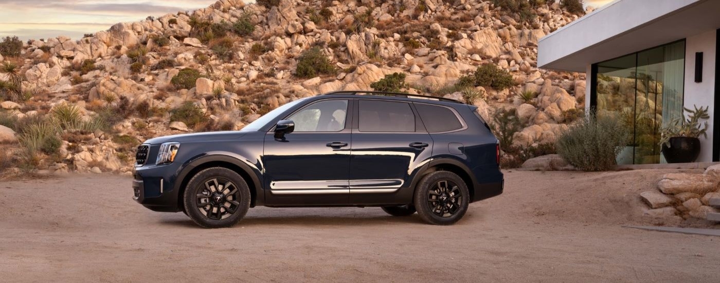 A black 2023 Kia Telluride is shown from the side near a modern home.