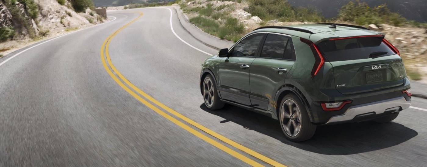 A green 2024 Kia Niro HEV is shown from the rear driving on an open road.