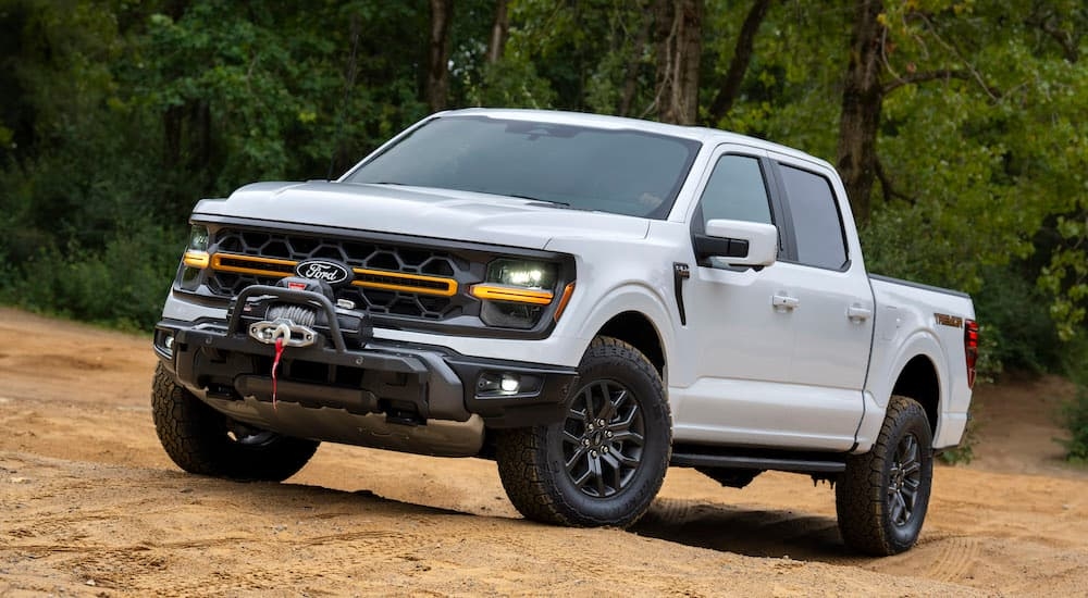 A white 2024 Ford F-150 Tremor is shown from the front at an angle while parked off-road after leaving a dealer that has a Ford trucks for sale.