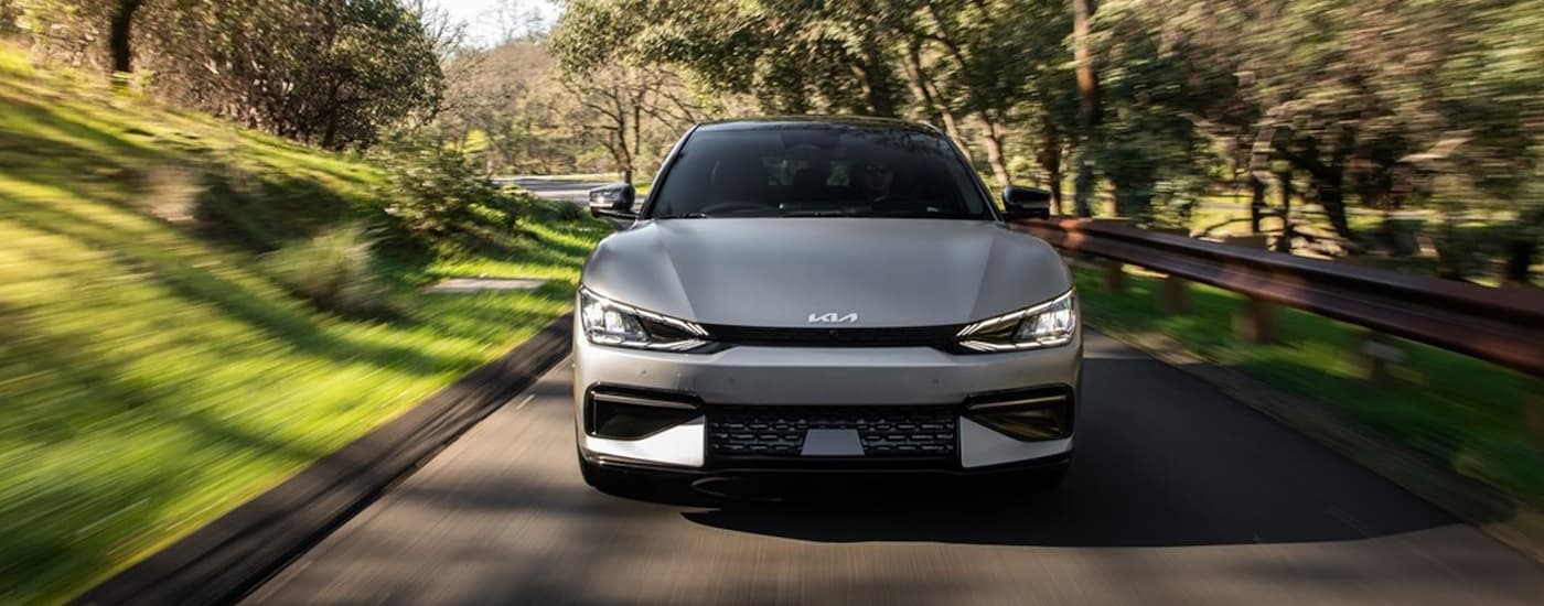 A silver 2023 Kia EV6 is shown from the front driving on tree-lined road after leaving a Houston Kia dealer.