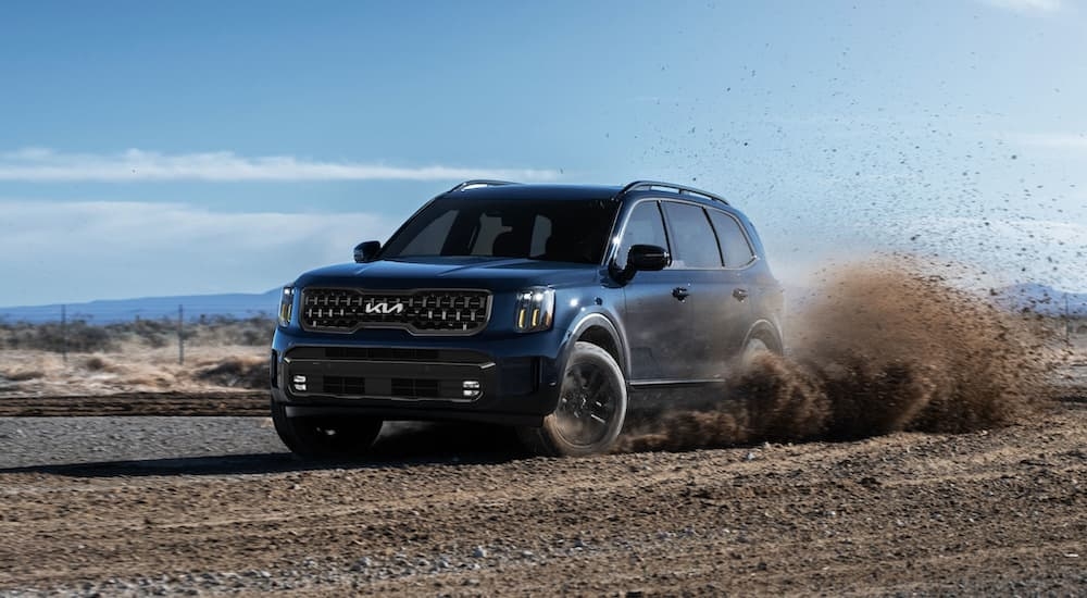 A blue 2024 Kia Telluride kicking up dirt on a track.