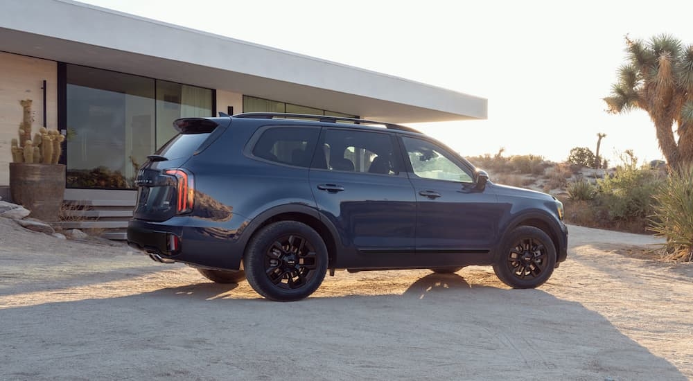 A blue 2024 Kia Telluride parked at a modern home in the desert.