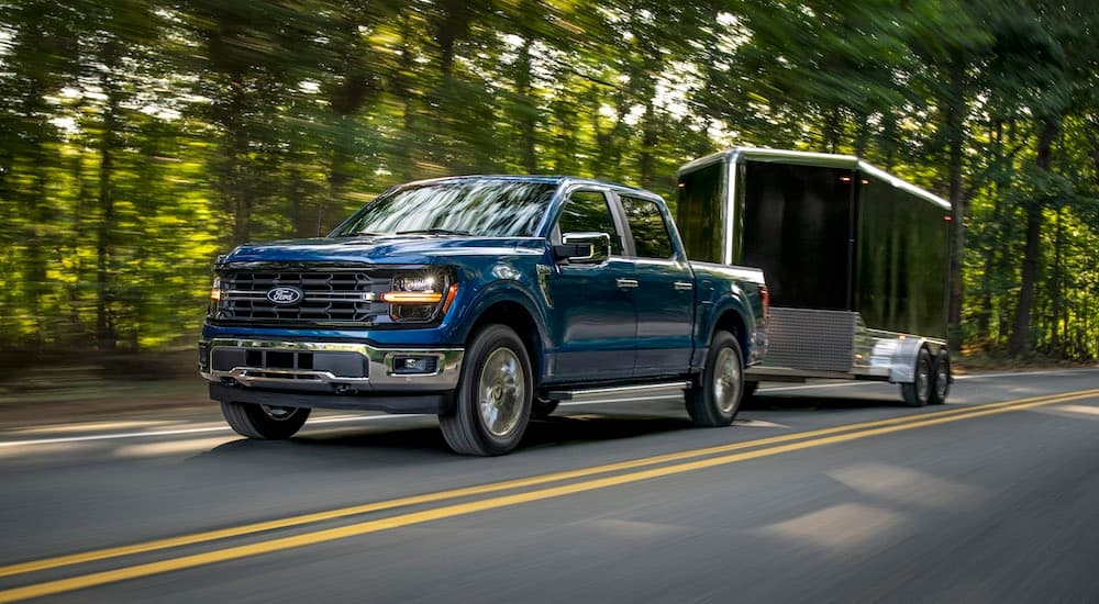 A blue 2024 Ford F-150 XLT is shown from the front at an angle while towing a trailer.