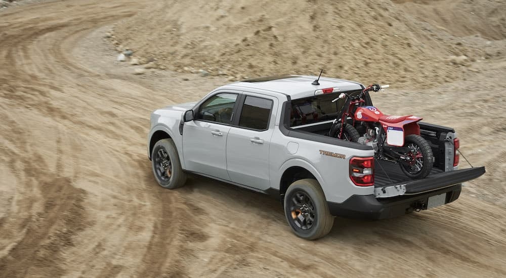 A grey 2024 Ford Maverick Tremor is shown from the rear at an angle while loaded with a dirt bike.