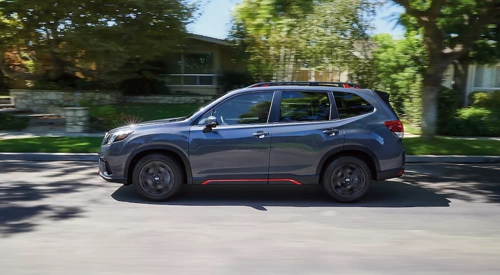 A grey 2024 Subaru Forester is shown from the side while driving on a city street after leaving a car dealership near Red Hook.