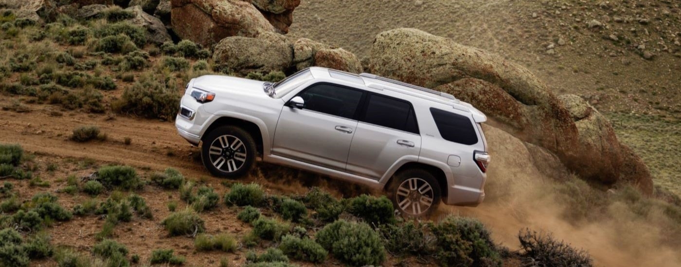 A white 2024 Toyota 4Runner Limited is shown from the side driving on a dusty trail.